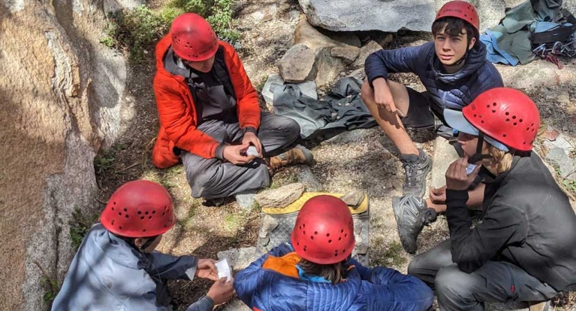 A group of students wearing helmets sit in a circle on the ground